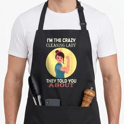 Cleaning housekeeper apron for women - Cartoon woman flexing in yellow circle with text I'M THE CRAZY CLEANING LADY — shown on a black cotton canvas apron against a white background