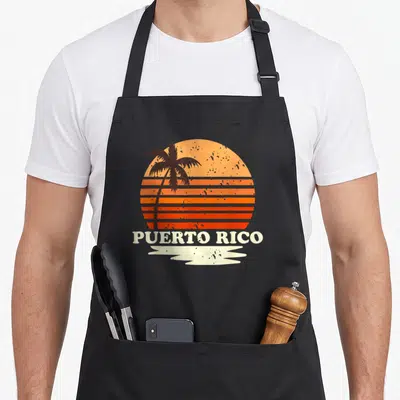 Rico 70s apron - Striped orange sunset with black palm tree and PUERTO RICO text above white brush stroke — shown on a black cotton canvas apron against a white background
