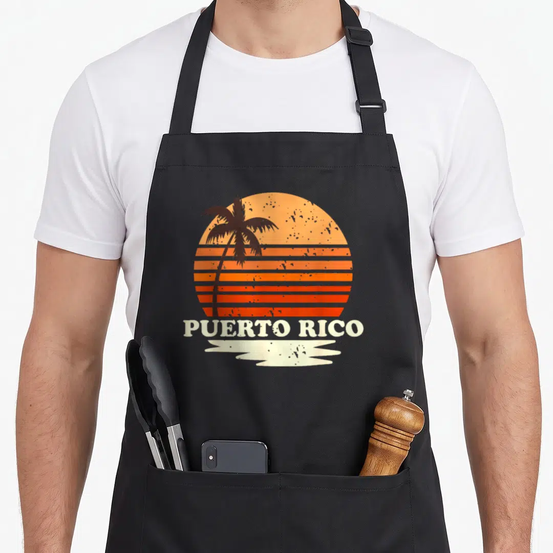 Rico 70s apron - Striped orange sunset with black palm tree and PUERTO RICO text above white brush stroke — shown on a black cotton canvas apron against a white background