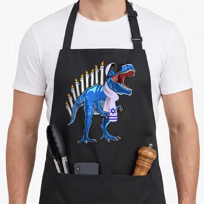 Menorasaurus hanukkah apron - Blue T-Rex with sunglasses and Star of David scarf in front of nine candles — shown on a black cotton canvas apron against a white background