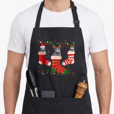Stocking russian aprons - Three grey cats in red and green stockings surrounded by string lights and snowflakes — shown on a black cotton canvas apron against a white background