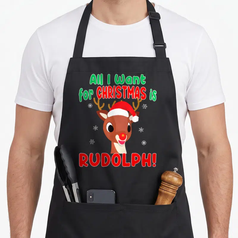 Nose reindeer red christmas apron - Rudolph reindeer head with Santa hat and All I Want for Christmas is Rudolph text — shown on a black cotton canvas apron against a white background