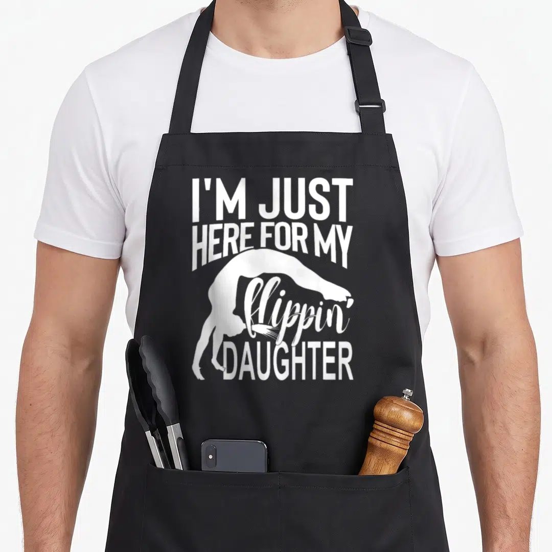 Flippin mom daughter apron - White gymnast backbend silhouette surrounded by stacked text reading I'm Just Here For My — shown on a black cotton canvas apron against a white background