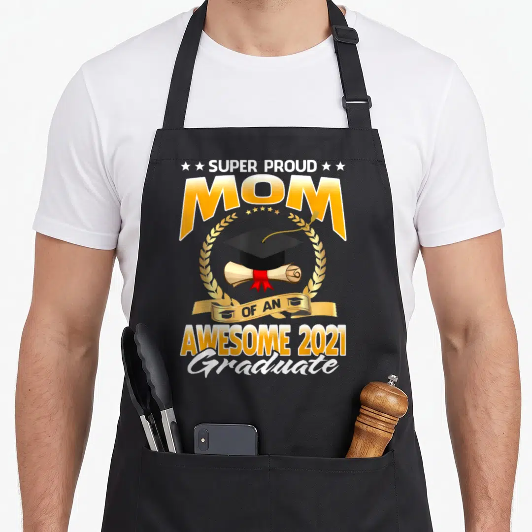 Funny proud graduate apron - Super Proud Mom Of An Awesome 2021 Graduate text with cap and diploma in gold wreath — shown on a black cotton canvas apron against a white background