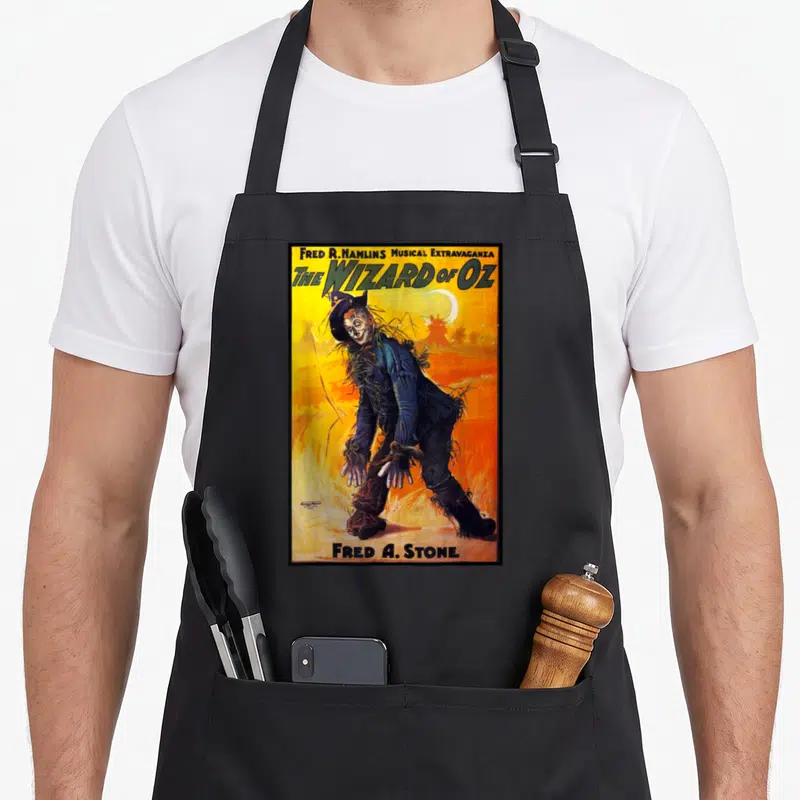 Poster scarecrow apron - Retro poster of Fred A. Stone as Scarecrow with yellow and orange background and crescent moon — shown on a black cotton canvas apron against a white background