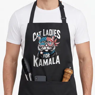 President cat lady apron - Realistic grey cat with patriotic sunglasses and CAT LADIES FOR KAMALA text — shown on a black cotton canvas apron against a white background