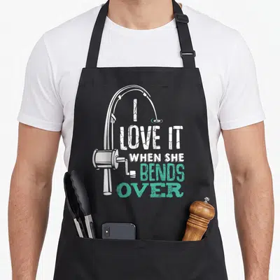 Angler fishing aprons - Distressed white and teal text I Love It When She Bends Over with a fishing rod graphic — shown on a black cotton canvas apron against a white background