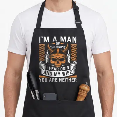 Fear wife apron - Orange skull in horned helmet flanked by candles and knotwork with white Norse text — shown on a black cotton canvas apron against a white background