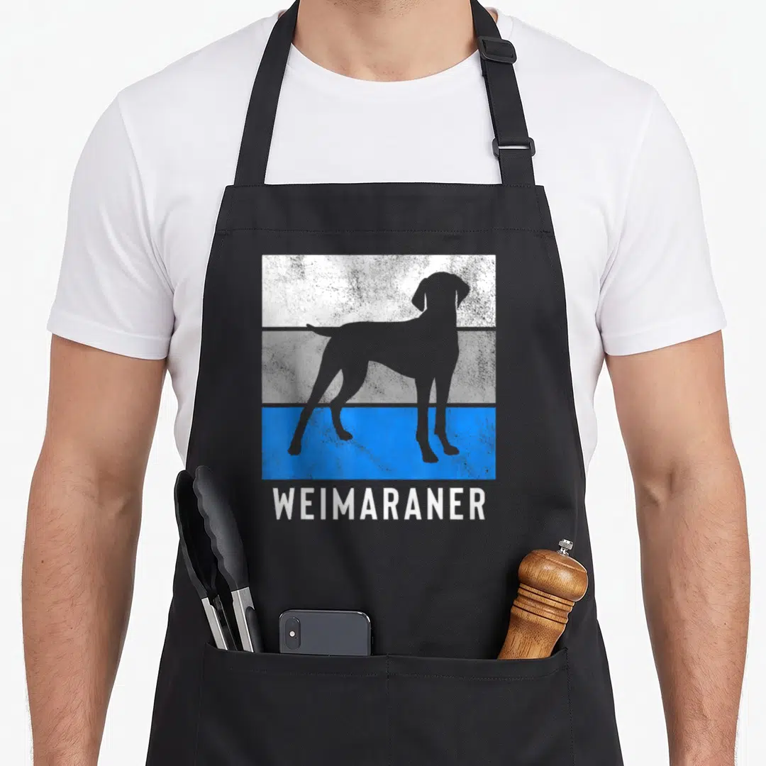 Cute weimaraner apron - Grey dog silhouette over white grey and blue stripes with WEIMARANER text below — shown on a black cotton canvas apron against a white background