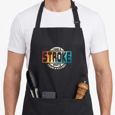 Cute survivor stroke awareness apron - I HAD A STROKE WHAT'S YOUR EXCUSE text in retro striped rectangle with arched — shown on a black cotton canvas apron against a white background