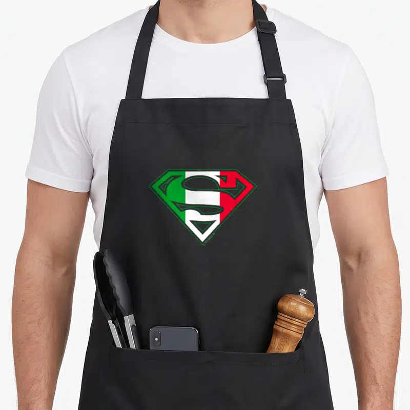 Shield italian apron - Superman shield logo filled with vertical green white and red stripes — shown on a black cotton canvas apron against a white background