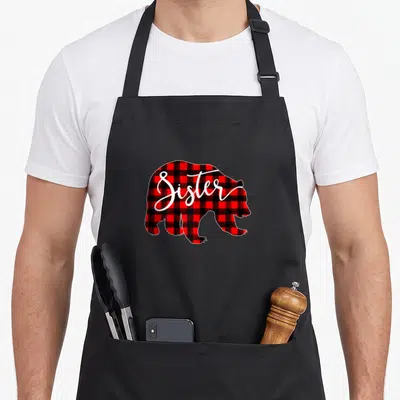 Sister buffalo plaid christmas apron - Red and black plaid bear silhouette with white Sister script — shown on a black cotton canvas apron against a white background