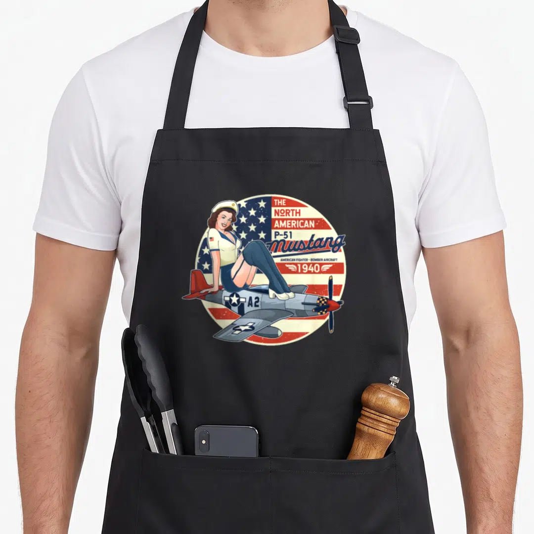 P51 airplane apron - Retro pin-up girl sitting on grey P-51 Mustang plane against circular USA flag with red white blue — shown on a black cotton canvas apron against a white background