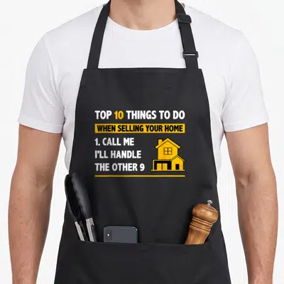 Realtor selling aprons - Top 10 things to do when selling your home text with yellow house icon — shown on a black cotton canvas apron against a white background