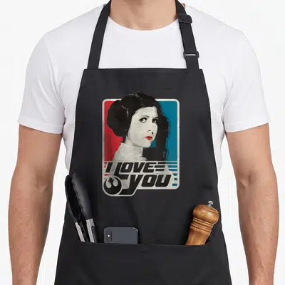 Rebel i love stars apron - Princess Leia portrait on red blue background with I LOVE YOU text and Rebel symbol — shown on a black cotton canvas apron against a white background