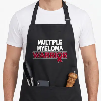 Cancer blood apron - White text MULTIPLE MYELOMA above red WARRIOR with ribbon replacing O — shown on a black cotton canvas apron against a white background
