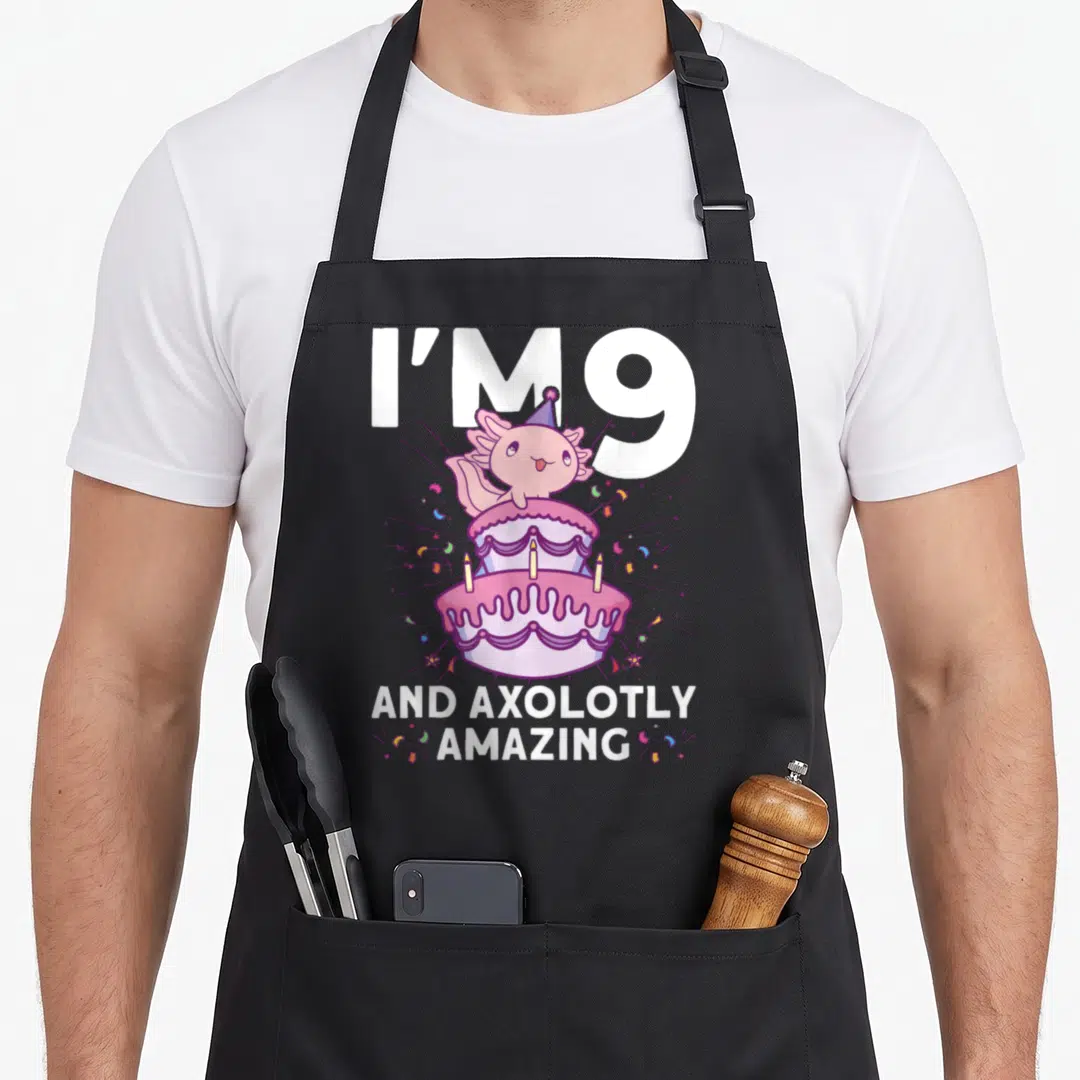 Axolotl 9th birthday apron - Pink axolotl on purple cake with I'm 9 and axolotly amazing text — shown on a black cotton canvas apron against a white background