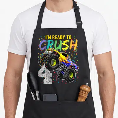Crush truck apron - I'M READY TO CRUSH 4 text with yellow monster truck and confetti — shown on a black cotton canvas apron against a white background