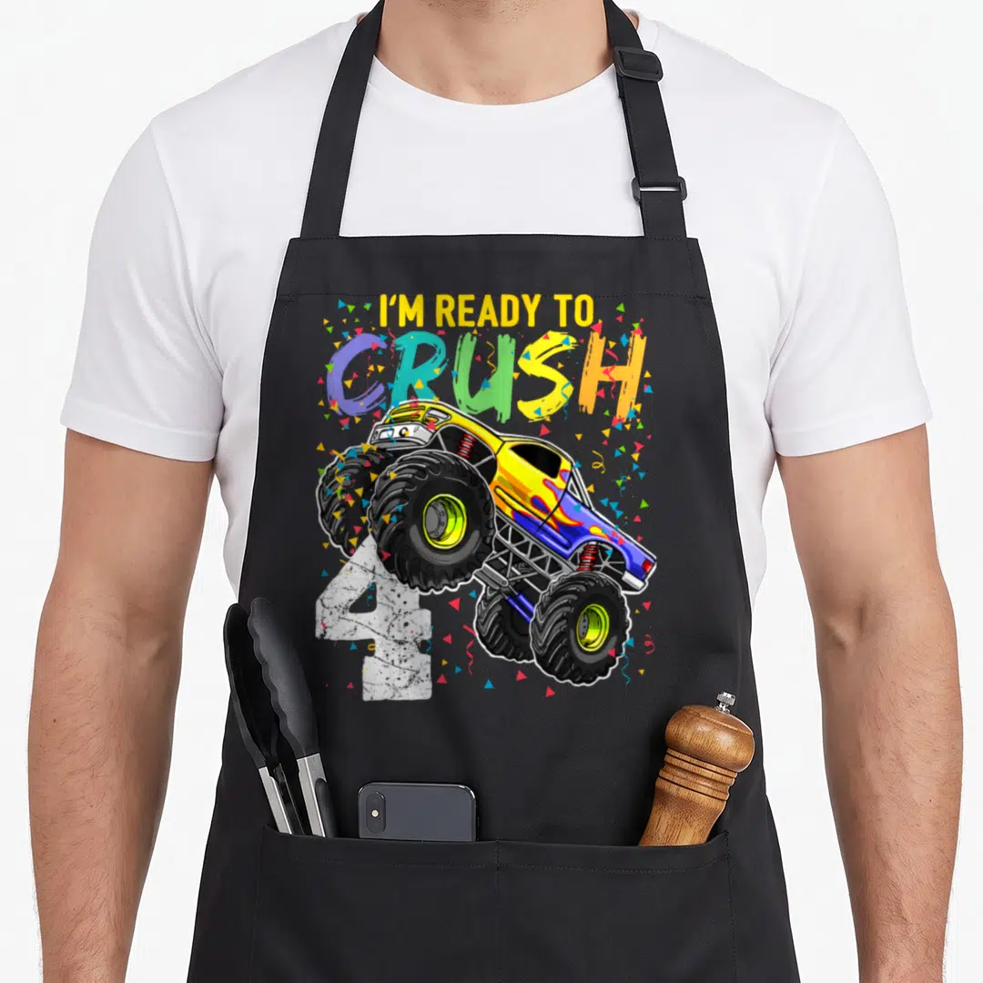 Crush truck apron - I'M READY TO CRUSH 4 text with yellow monster truck and confetti — shown on a black cotton canvas apron against a white background