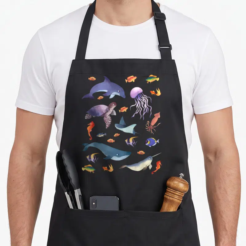 Biology animal apron - Watercolor sea creatures in blue purple orange yellow scattered cluster design — shown on a black cotton canvas apron against a white background