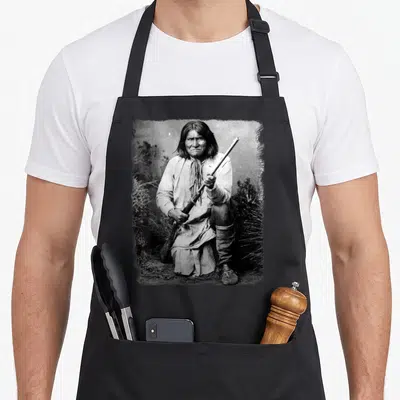 Geronimo native american apron - Grayscale photo of seated man holding rifle in traditional attire — shown on a black cotton canvas apron against a white background