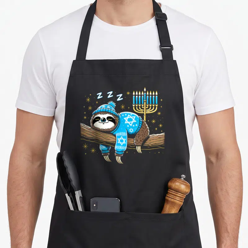 Sloth hanukkah apron - Cartoon sloth sleeping on branch wearing blue star patterned sweater next to golden menorah — shown on a black cotton canvas apron against a white background