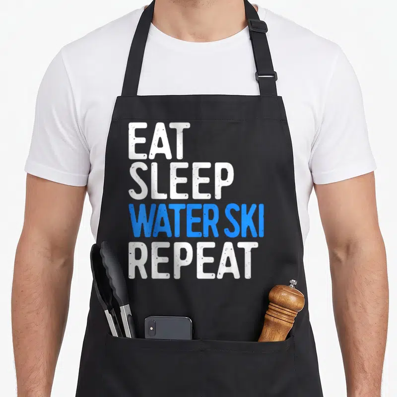 Eat water skiing apron - Stacked white and blue text reading EAT SLEEP WATER SKI REPEAT — shown on a black cotton canvas apron against a white background