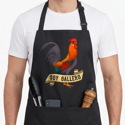 Soy chicken apron - Cartoon rooster in red orange grey feathers standing behind beige banner with soy gallero text — shown on a black cotton canvas apron against a white background