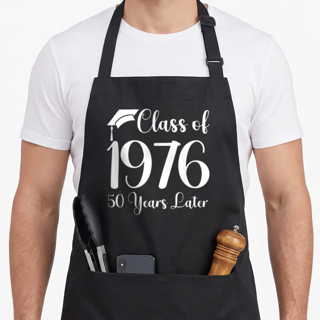 Later class reunion apron - White Class of 1976 50 Years Later text with graduation cap icon — shown on a black cotton canvas apron against a white background
