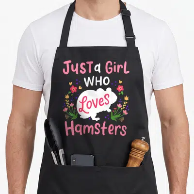 Funny love hamsters apron - Cartoon hamster with pink text and floral dots — shown on a black cotton canvas apron against a white background