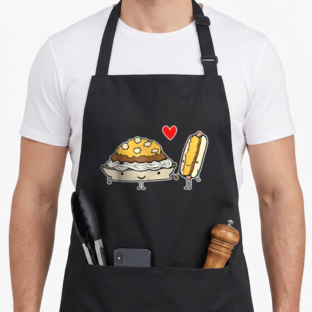 Cincinnati chili aprons - Cartoon noodle bowl and hot dog holding hands with red heart — shown on a black cotton canvas apron against a white background