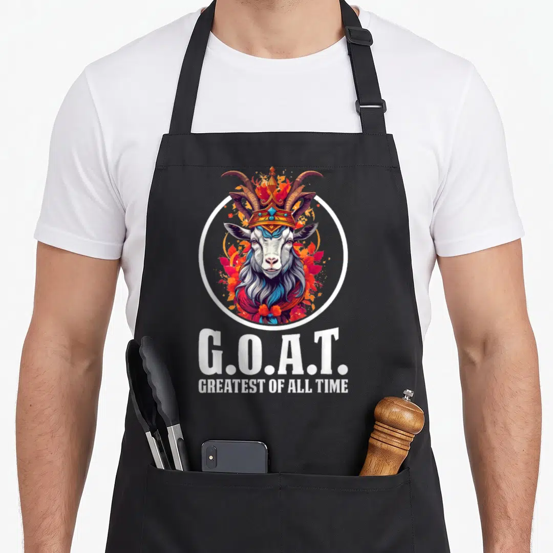 Funny greatest of all time apron - Crowned goat head inside white circle with autumn leaves and stacked G.O.A.T. text — shown on a black cotton canvas apron against a white background