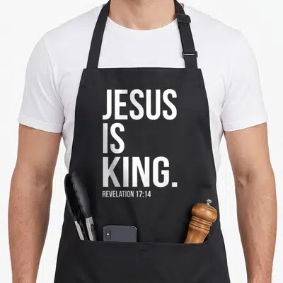Bible king of the grill apron - White stacked text JESUS IS KING. and REVELATION 17:14 on dark background — shown on a black cotton canvas apron against a white background