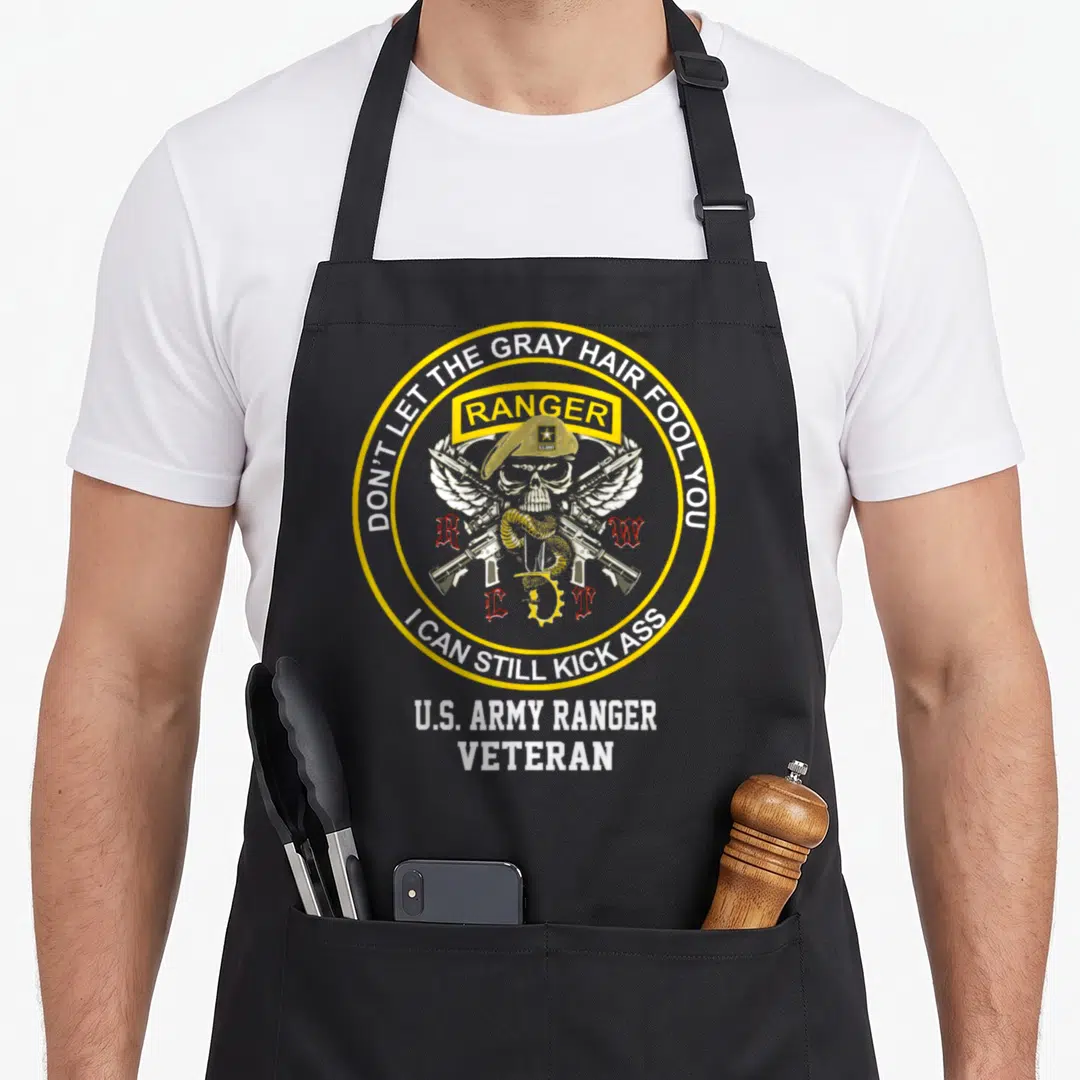 Ranger military apron - Skull in beret with crossed rifles and text Don't Let The Gray Hair Fool You inside yellow — shown on a black cotton canvas apron against a white background