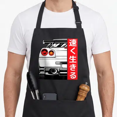 Drifting design imports vintage apron - Rear of white cartoon car next to red vertical bar with white Japanese — shown on a black cotton canvas apron against a white background