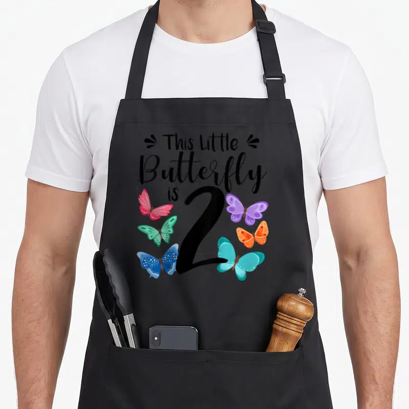 Birthday 2nd butterfly aprons - This Little Butterfly is 2 text with six colorful cartoon butterflies and decorative — shown on a black cotton canvas apron against a white background