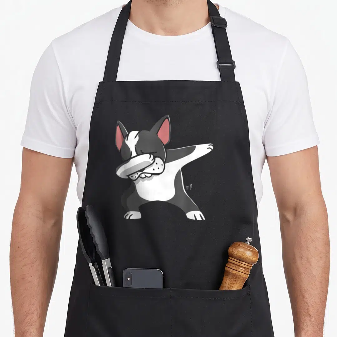 Dabbing beans lover apron - Cartoon black and white Boston Terrier dog dabbing with pink inner ears on grey background — shown on a black cotton canvas apron against a white background