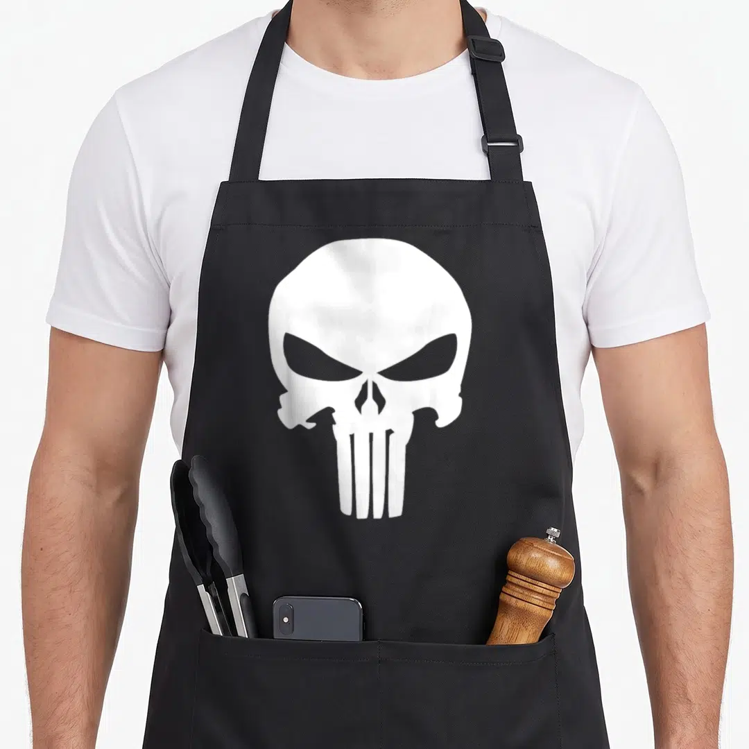 Punisher skull apron - White minimalist skull graphic centered on canvas fabric with two front pockets — shown on a black cotton canvas apron against a white background