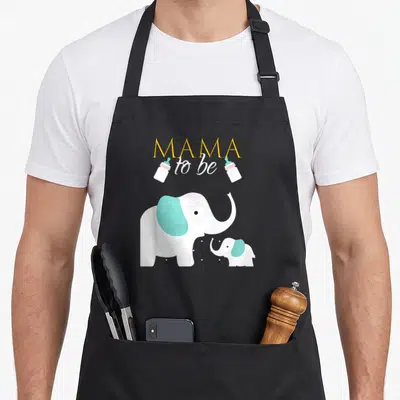 Elephant mama apron - MAMA to be text with two bottles and white cartoon elephants with blue ears — shown on a black cotton canvas apron against a white background