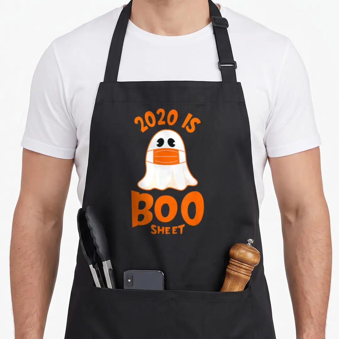 Boo sheet halloween apron - Cartoon ghost wearing an orange mask under arched 2020 IS BOO SHEET text — shown on a black cotton canvas apron against a white background