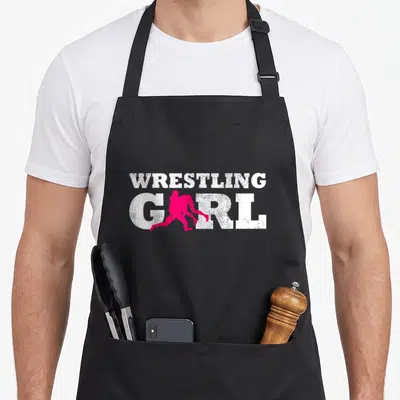 Silhouette wrestling apron - WRESTLING GIRL white text with pink wrestler silhouette replacing the letter I on black — shown on a black cotton canvas apron against a white background
