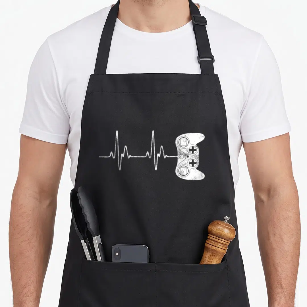 Heartbeat gaming apron - White distressed game controller connected to a heartbeat EKG line on black fabric — shown on a black cotton canvas apron against a white background