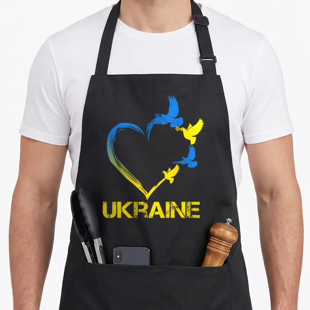 Retro ukraine ukrainian aprons - Blue and yellow heart brushstrokes with four flying doves and UKRAINE text — shown on a black cotton canvas apron against a white background