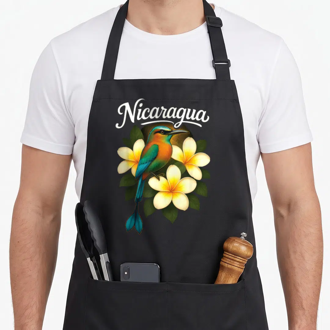 Guardabarranco nicaraguan girl apron - Nicaragua text over realistic motmot bird and plumeria flowers in blue and orange — shown on a black cotton canvas apron against a white background