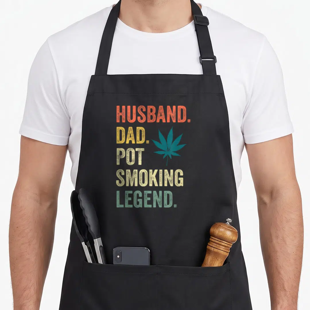 Stoner smoker apron - Stacked HUSBAND DAD POT SMOKING LEGEND text with teal cannabis leaf in retro colors — shown on a black cotton canvas apron against a white background