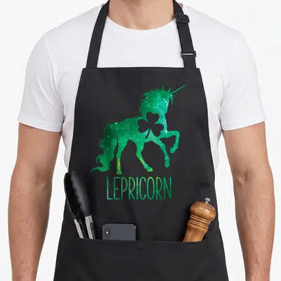Lepricorn st patrick day aprons - Green galaxy unicorn silhouette with shamrock cutout and LEPRICORN text — shown on a black cotton canvas apron against a white background