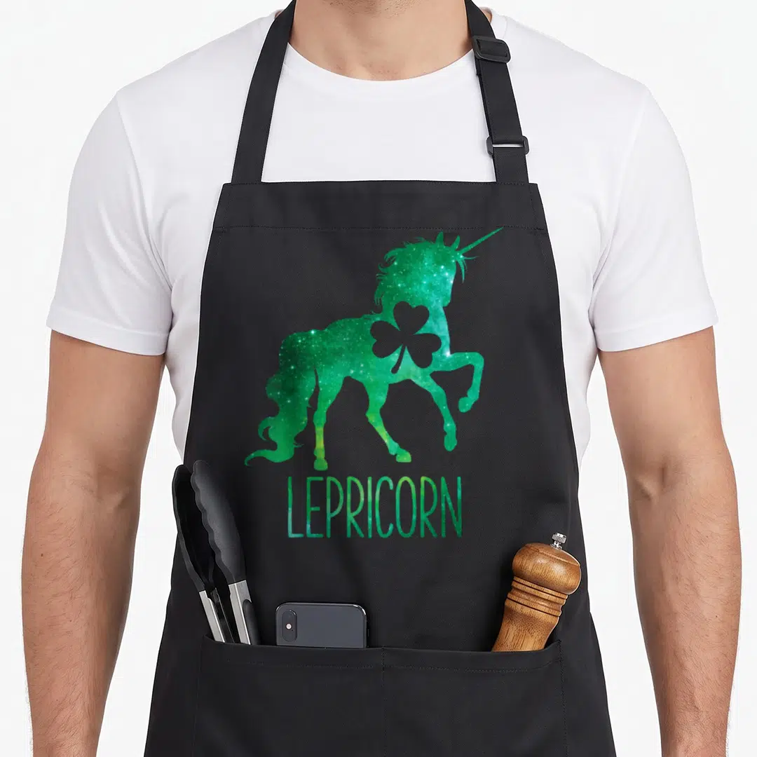 Lepricorn st patrick day aprons - Green galaxy unicorn silhouette with shamrock cutout and LEPRICORN text — shown on a black cotton canvas apron against a white background