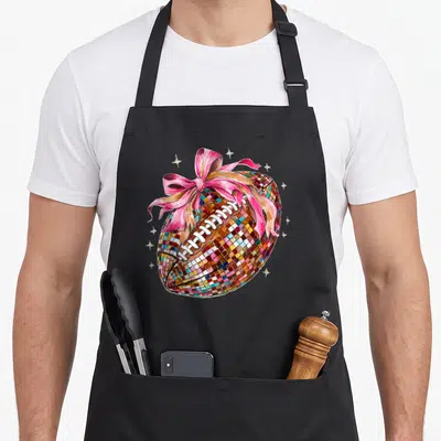 Disco bow apron - Mosaic football with pink bow and gold stars cartoon design — shown on a black cotton canvas apron against a white background