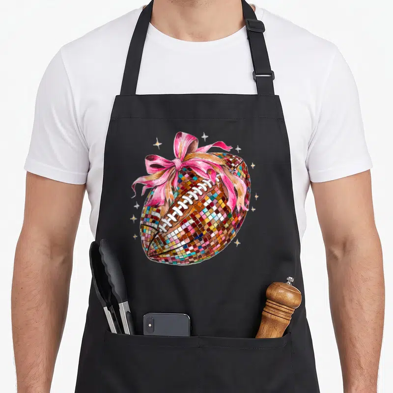 Disco bow apron - Mosaic football with pink bow and gold stars cartoon design — shown on a black cotton canvas apron against a white background