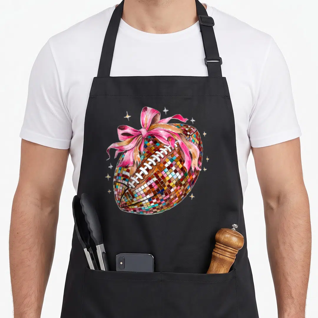 Disco bow apron - Mosaic football with pink bow and gold stars cartoon design — shown on a black cotton canvas apron against a white background
